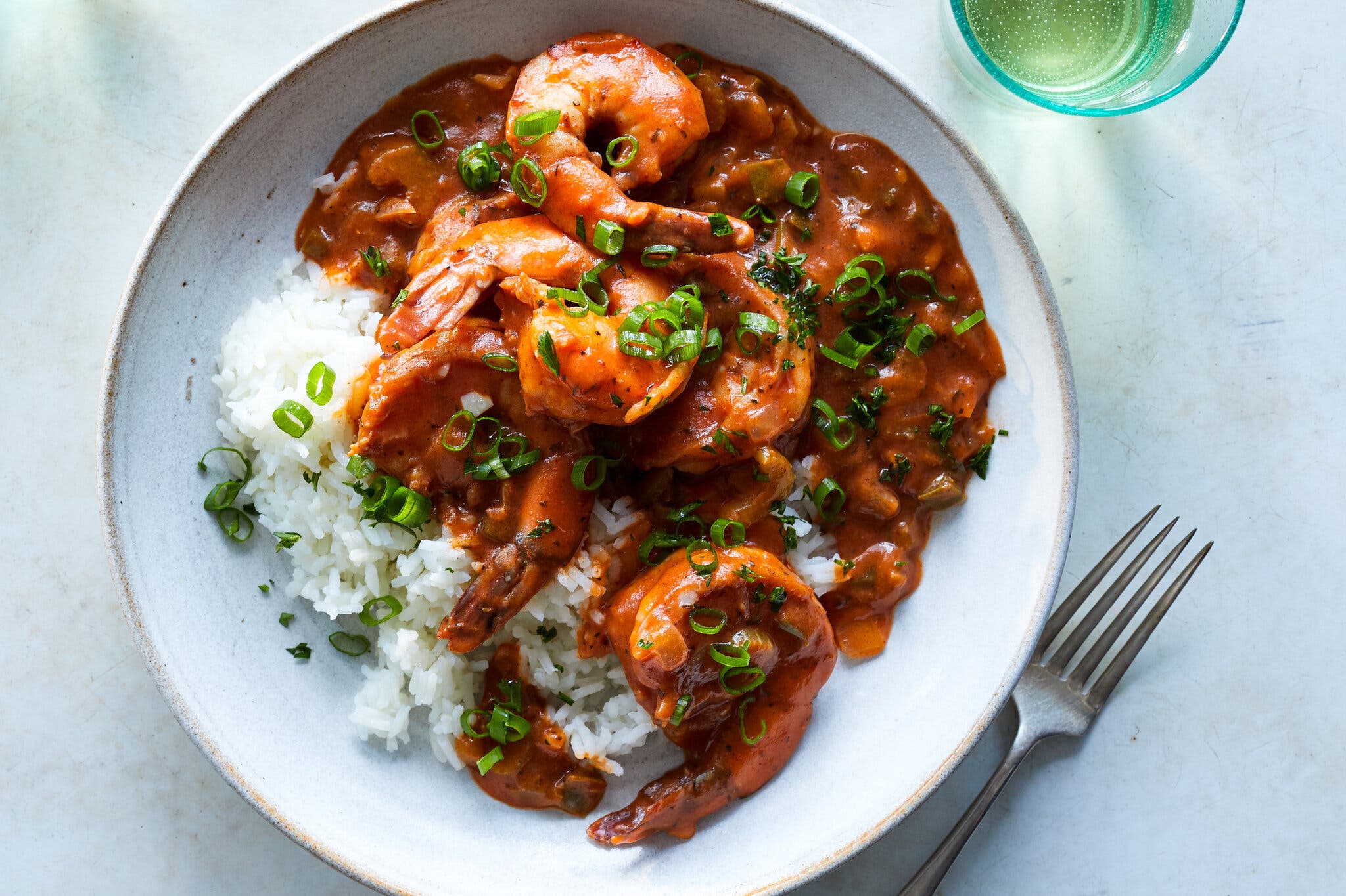 Shrimp in brick red sauce is set over white rice in a white bowl.