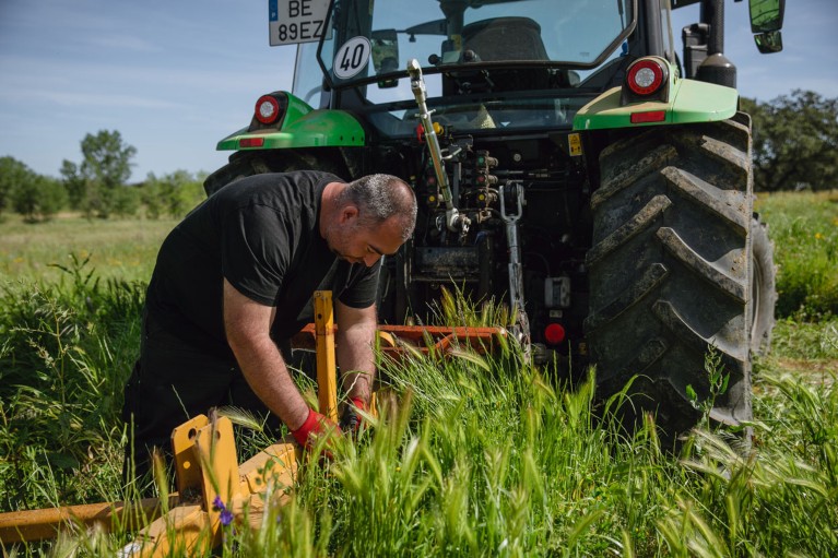 A farmer attaches an apparatus to the back of a green tractor in a grassy field