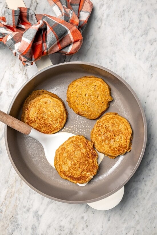 Overhead view of spatula flipping pumpkin pancake in skillet
