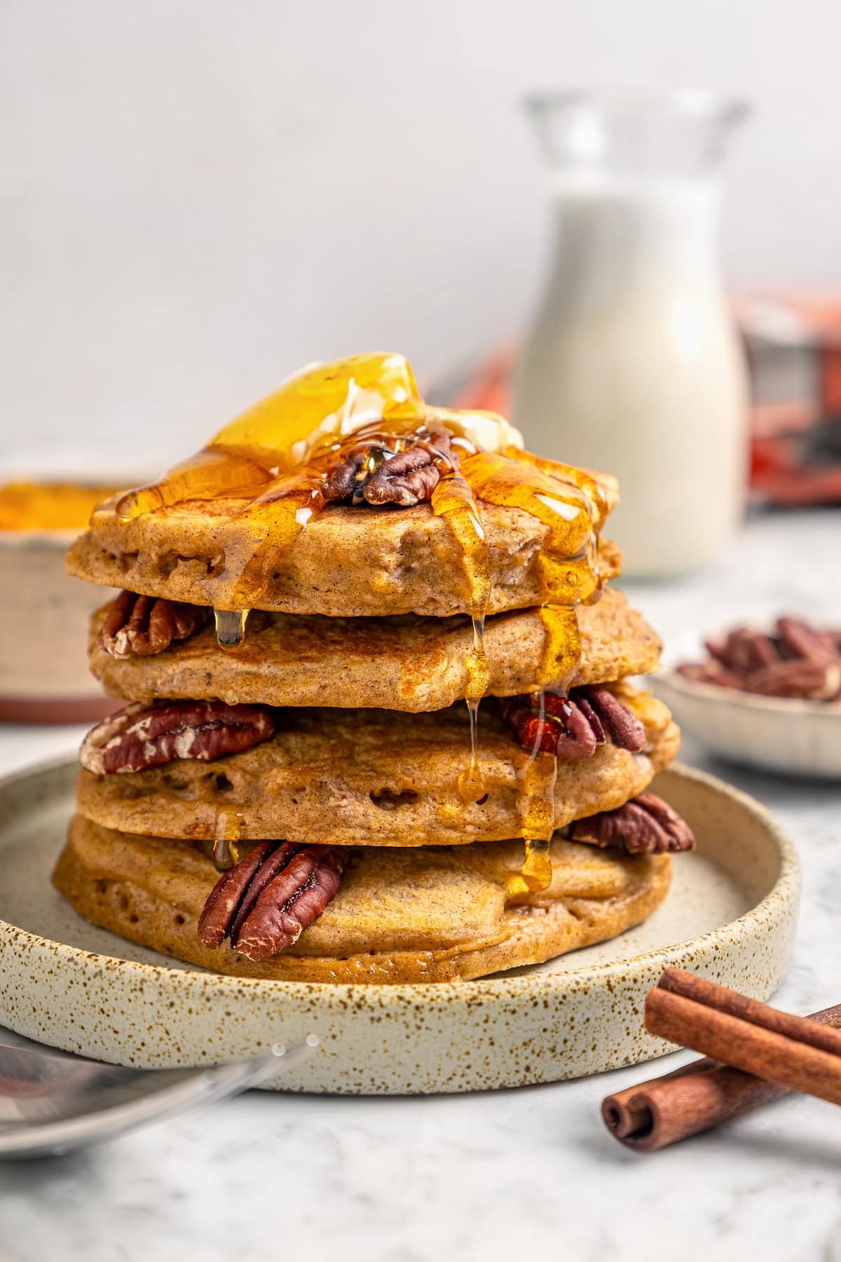 Stack of pumpkin pancakes on plate with syrup, pecans, and butter