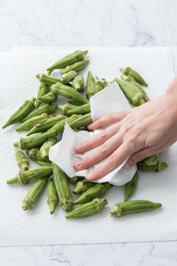 Patting dry okra with a paper towel.