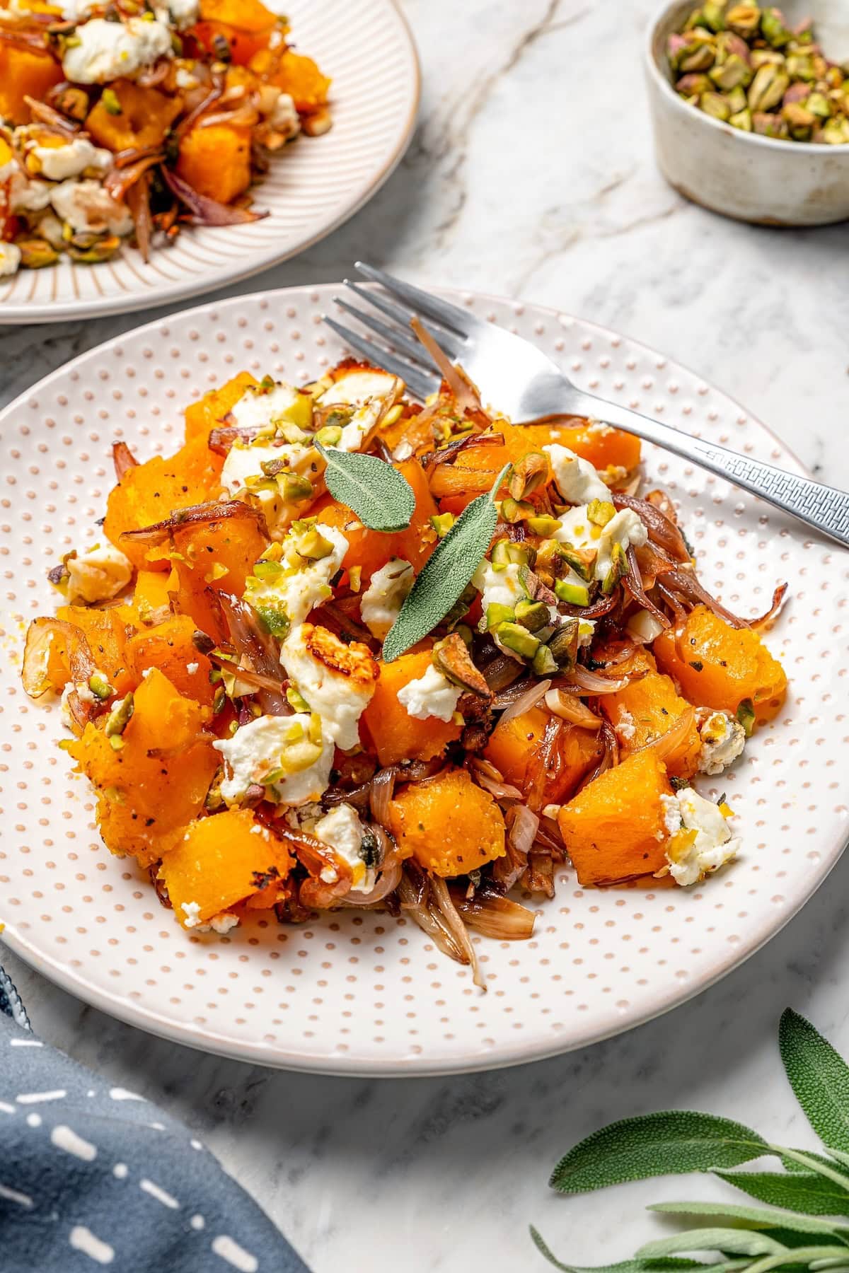 Butternut squash bake on plate with goat cheese, pistachios, and sage.
