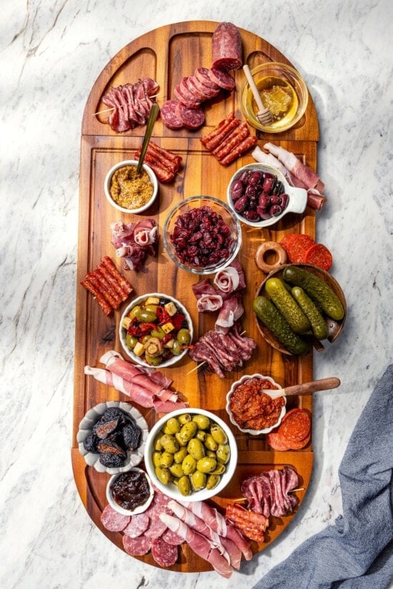 Your ultimate guide to creating a charcuterie and cheese board! I'll show you how to choose and arrange everything for a beautiful spread. Charcuterie board in process, with bowls and meats.