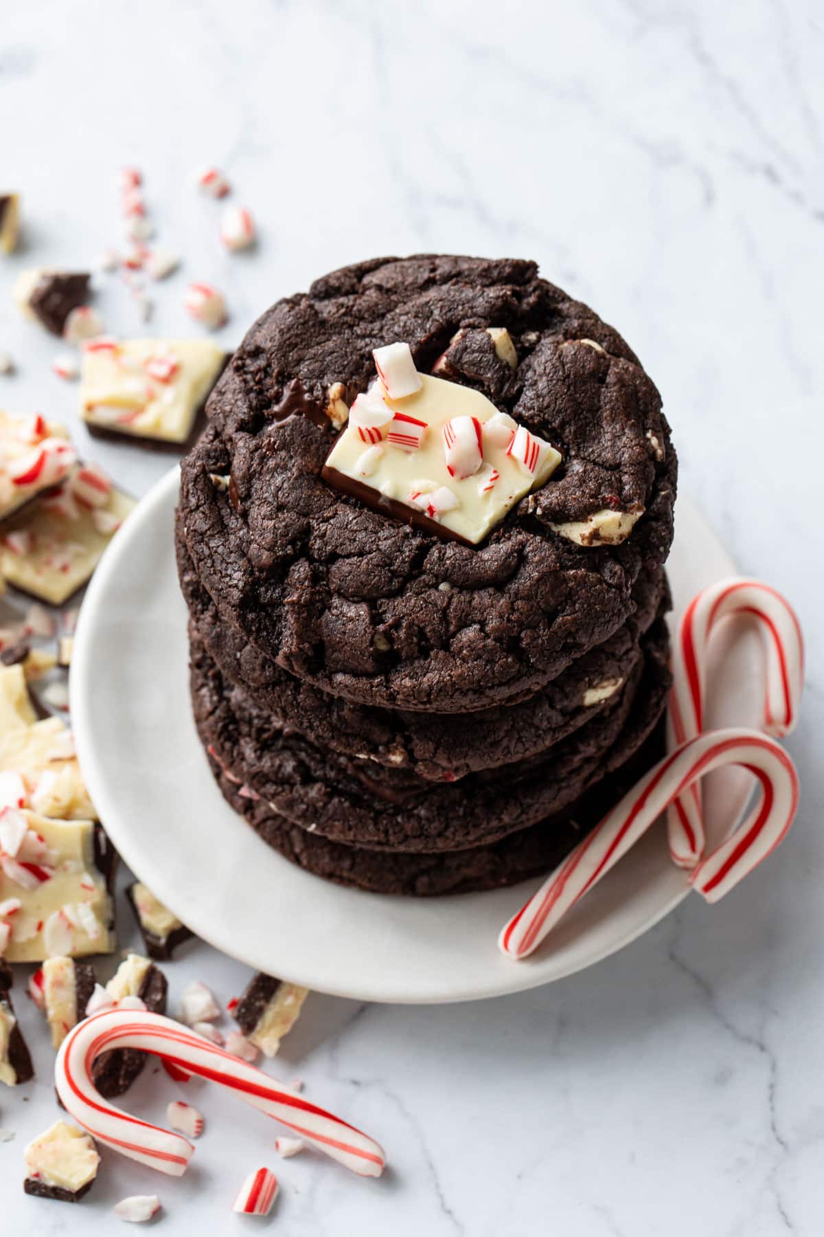 Top down view of a stack of Chocolate Peppermint Bark Cookies on a small white cookie plate with two candy canes on the side.
