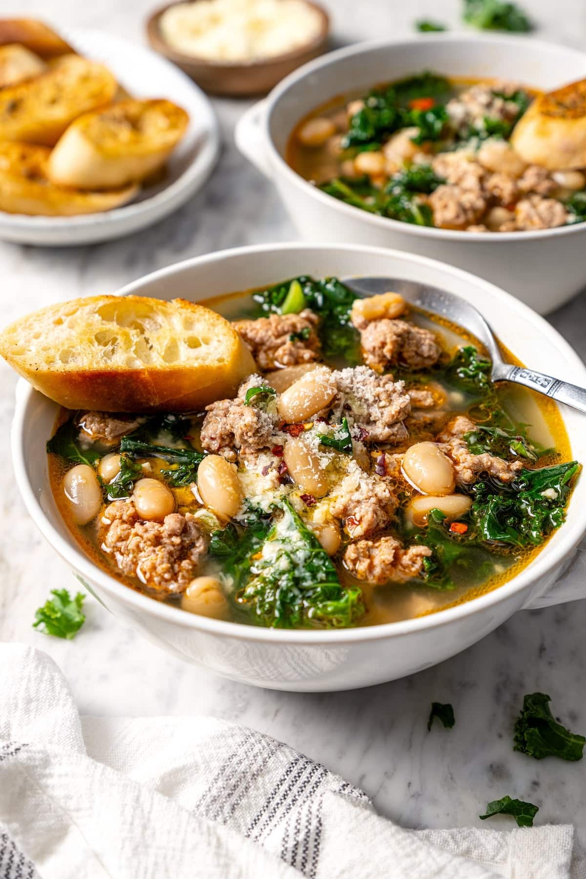 Spoon and toast in bowl of white bean soup with sausage and kale.