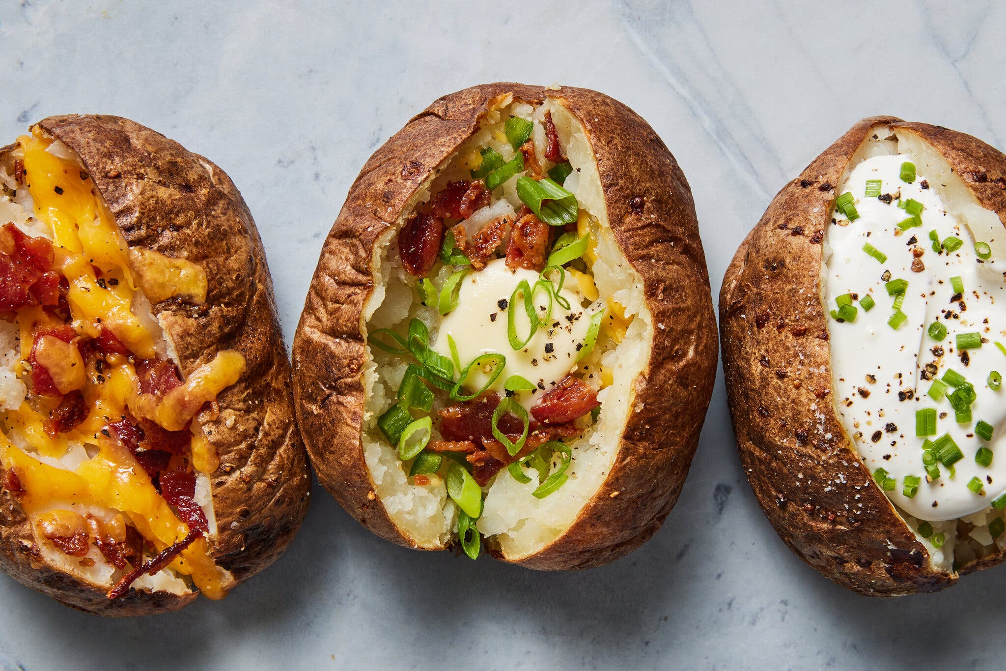 Three baked potatoes with different toppings: bacon and cheese, sour cream and chives.