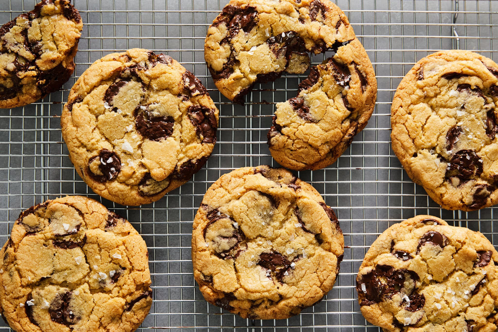 Thick chocolate chip cookies topped with sea salt on a wire cooling rack.