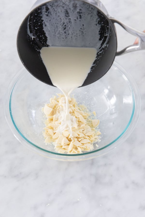 Pouring warmed cream over chopped white chocolate in a mixing bowl.
