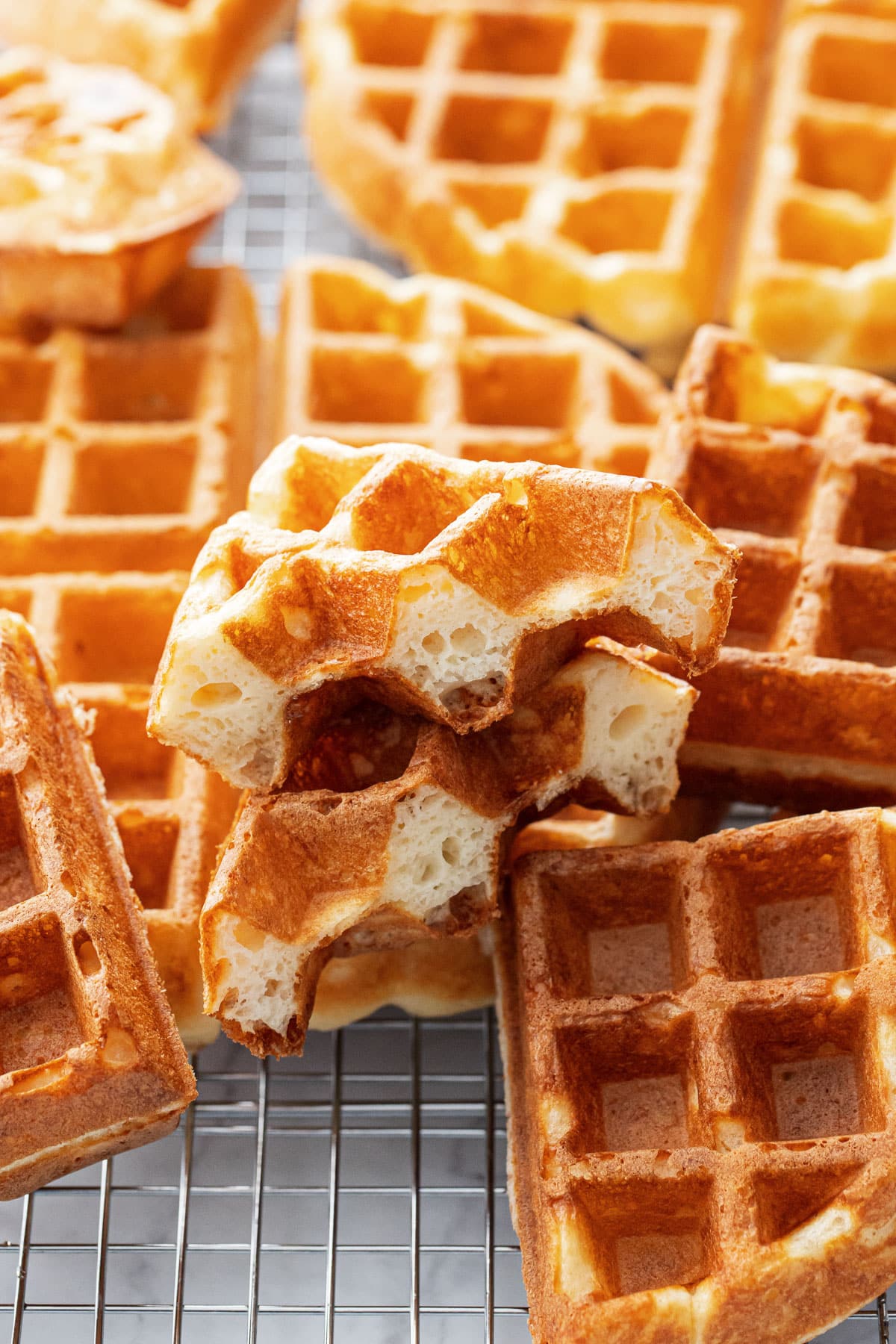Golden brown Overnight Sourdough Discard Waffles on a wire baking rack, one waffle cut to show the fluffy interior texture.